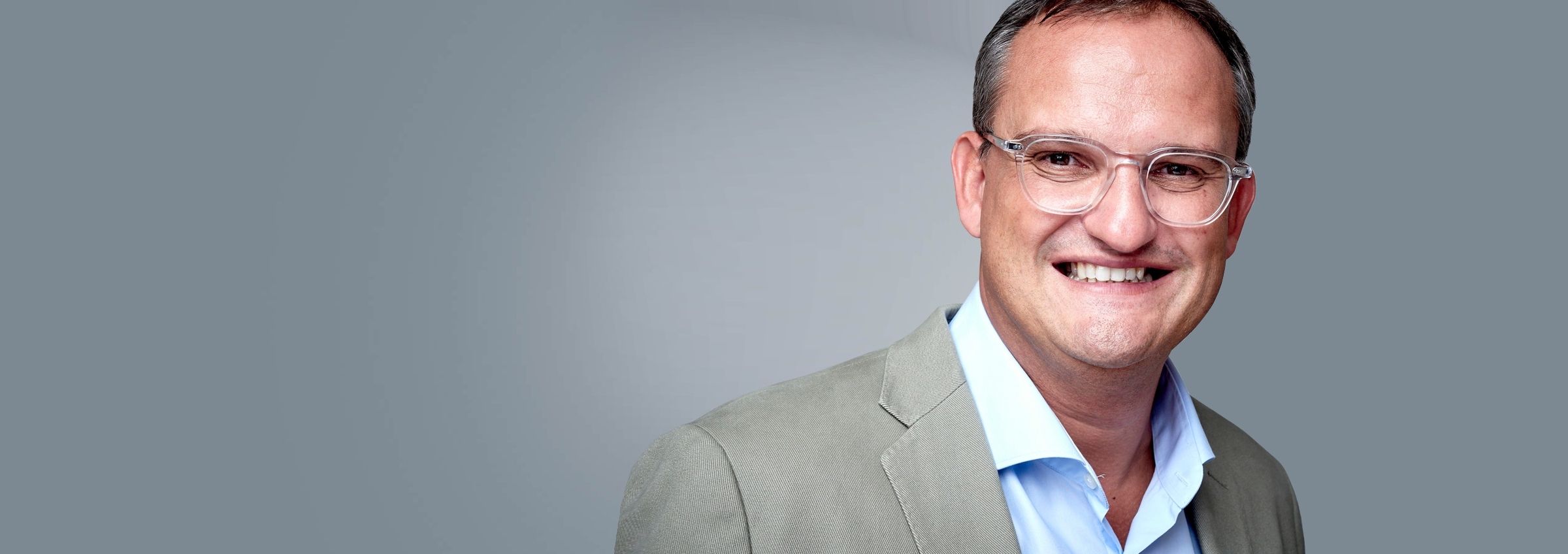 Dr. med. univ. Reinhard Kaliwoda in einem eleganten Anzug, Brille und einem freundlichem Lächeln